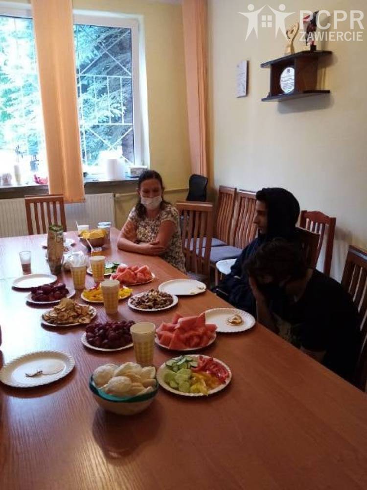 Zdjęcie: Trzy osoby siedzą przy stole, na którym w pojemnikach poustawiane są pokrojone produkty spożywcze